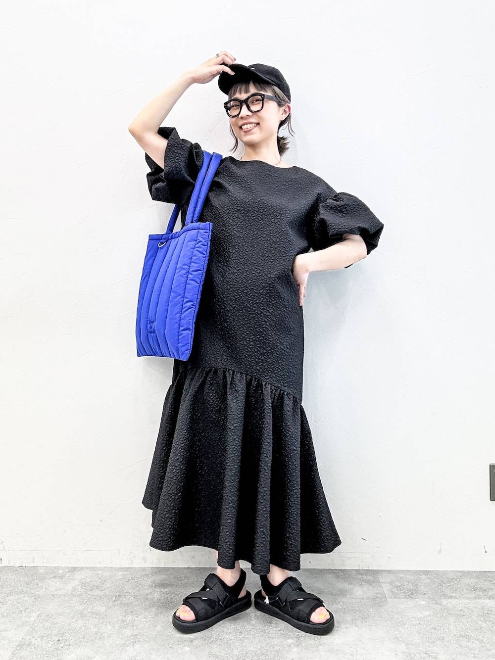 ブラック系のサンダル、ブルー系のトートバッグ、ブラック系のキャップを着用したレディースの春コーディネートの1枚目の写真