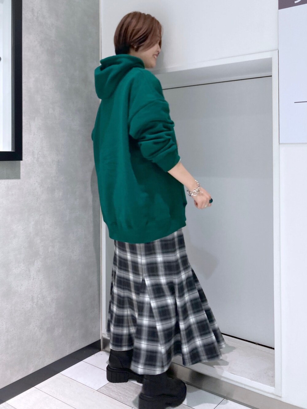 グリーン系のパーカー、ブラック系のスカート、ブラック系のブーツを着用したレディースの冬コーディネートの2枚目の写真