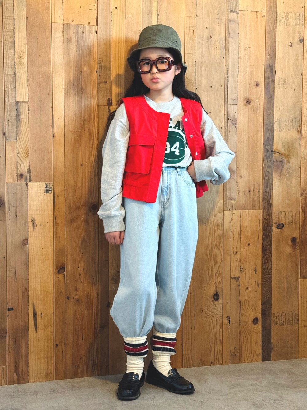 レッド系のベスト、グレー系のスウェット、ブルー系のデニムパンツを着用したキッズの冬コーディネートの1枚目の写真