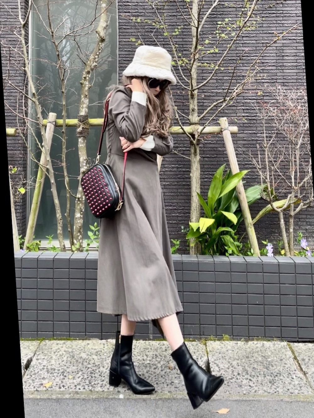 グレー系のワンピース、ブラック系のショルダーバッグ、ブラック系のブーツを着用したレディースの春コーディネートの1枚目の写真