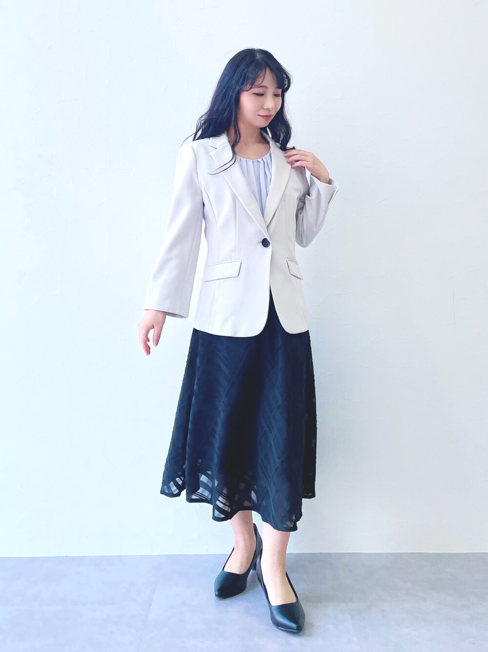 ブラック系のスカート、ブラック系のパンプス、グレー系のジャケット/アウターを着用したレディースの春コーディネートの1枚目の写真