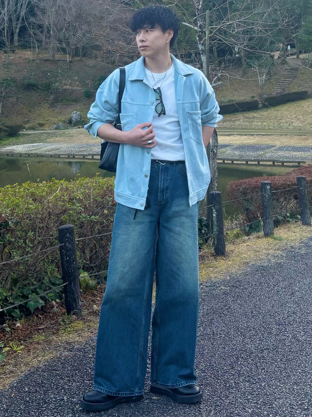 ブルー系のデニムパンツ、ブラック系のショルダーバッグ、ブラック系のドレスシューズを着用したメンズの春コーディネートの1枚目の写真