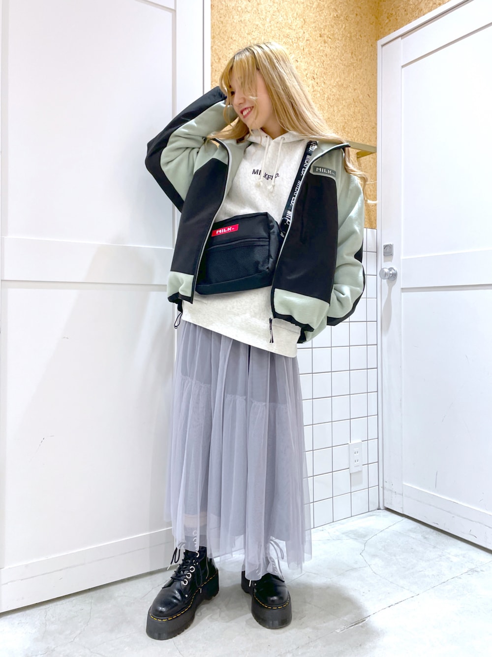 グレー系のスカート、ホワイト系のパーカー、グリーン系のブルゾンを着用したレディースの秋コーディネートの1枚目の写真