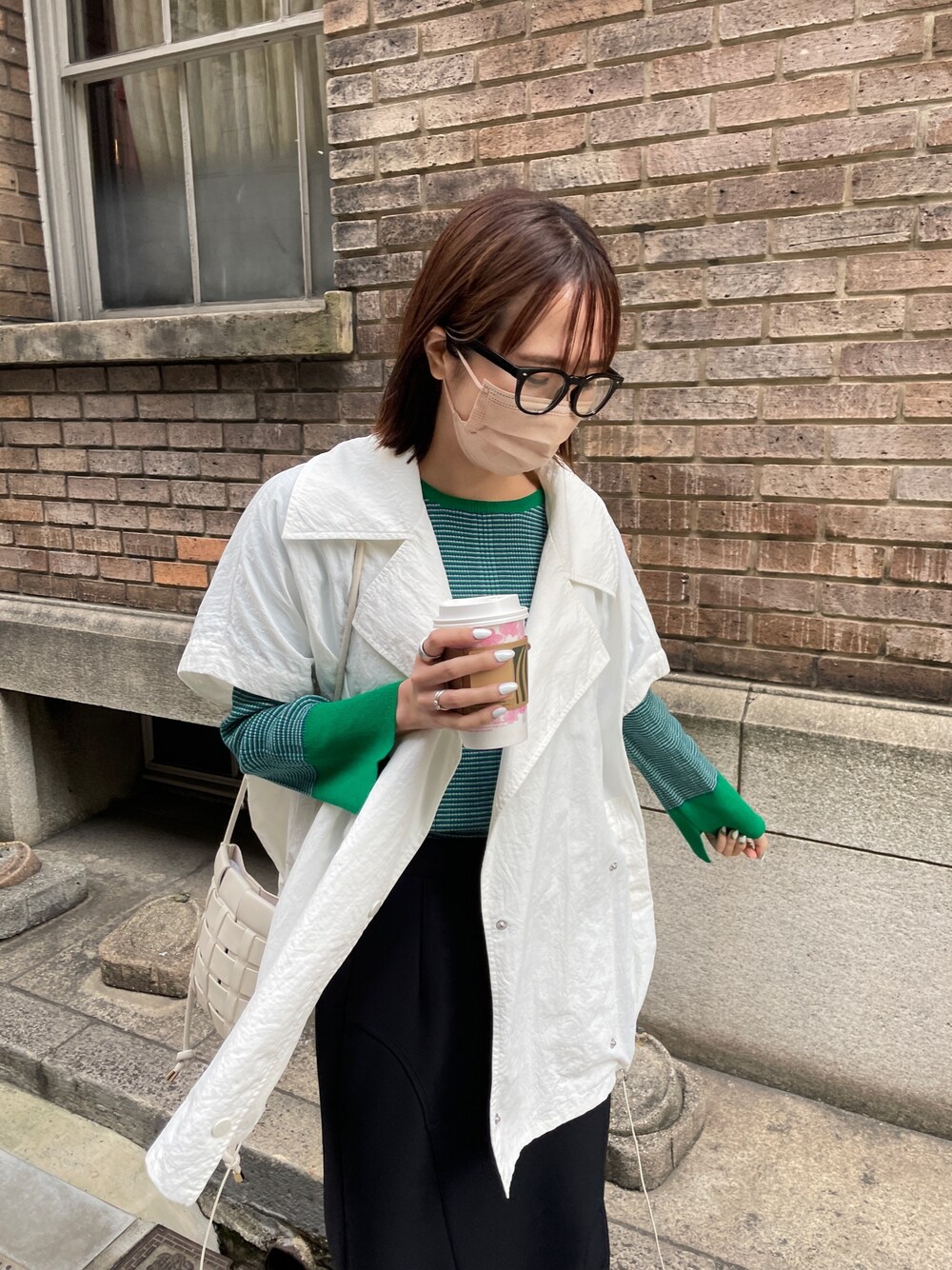 グリーン系のニット/セーター、ホワイト系のブルゾン、ブラック系のスカートを着用したレディースの春コーディネートの2枚目の写真