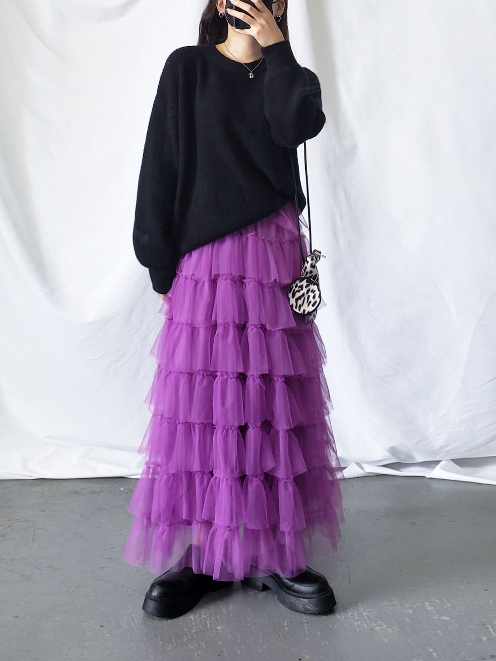 パープル系のスカート、ブラック系のニット/セーター、ブラック系のショルダーバッグを着用したレディースの夏コーディネートの1枚目の写真