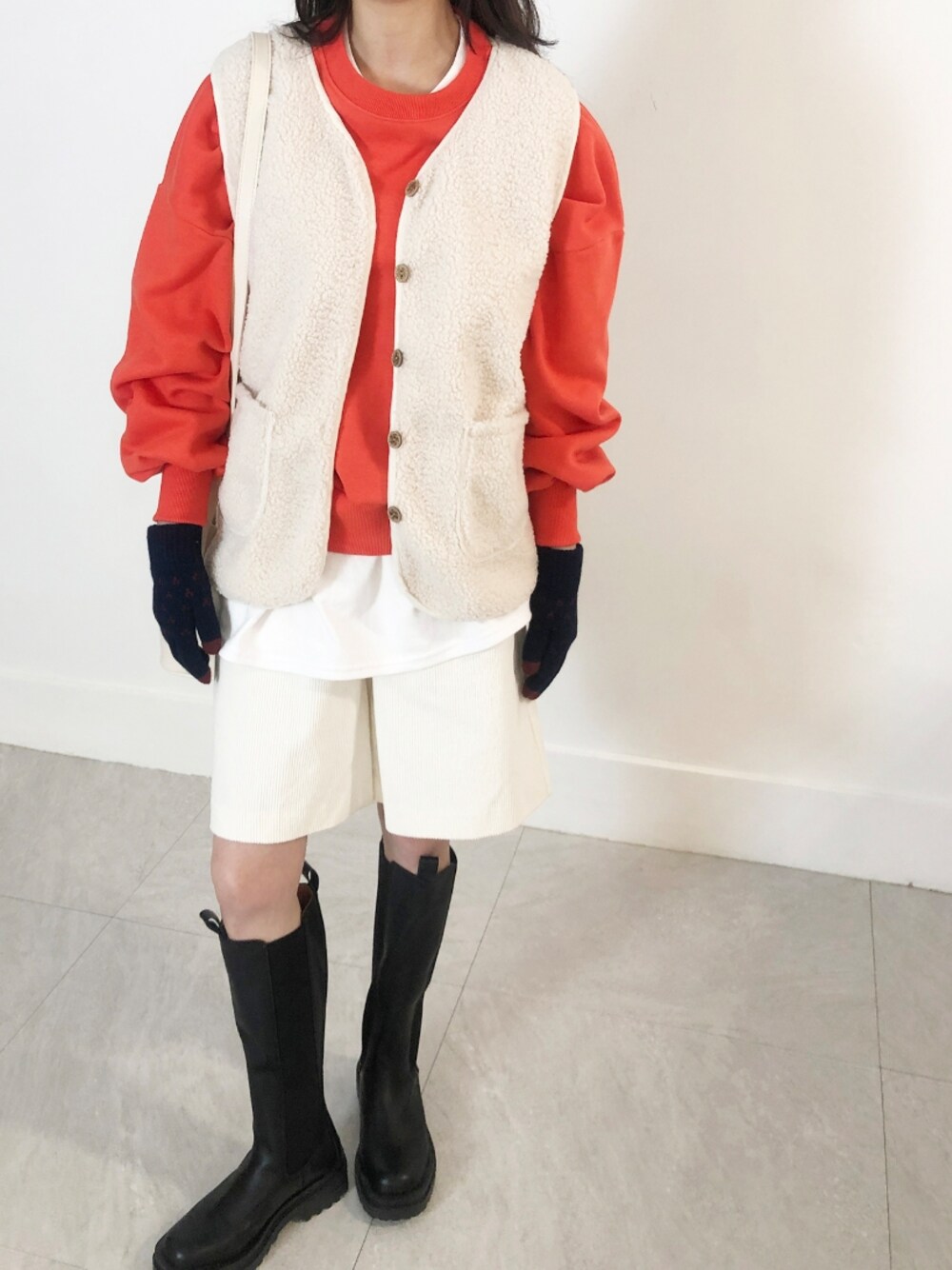 オレンジ系のスウェット、ホワイト系のベスト、ブラック系の手袋を着用したレディースの冬コーディネートの1枚目の写真