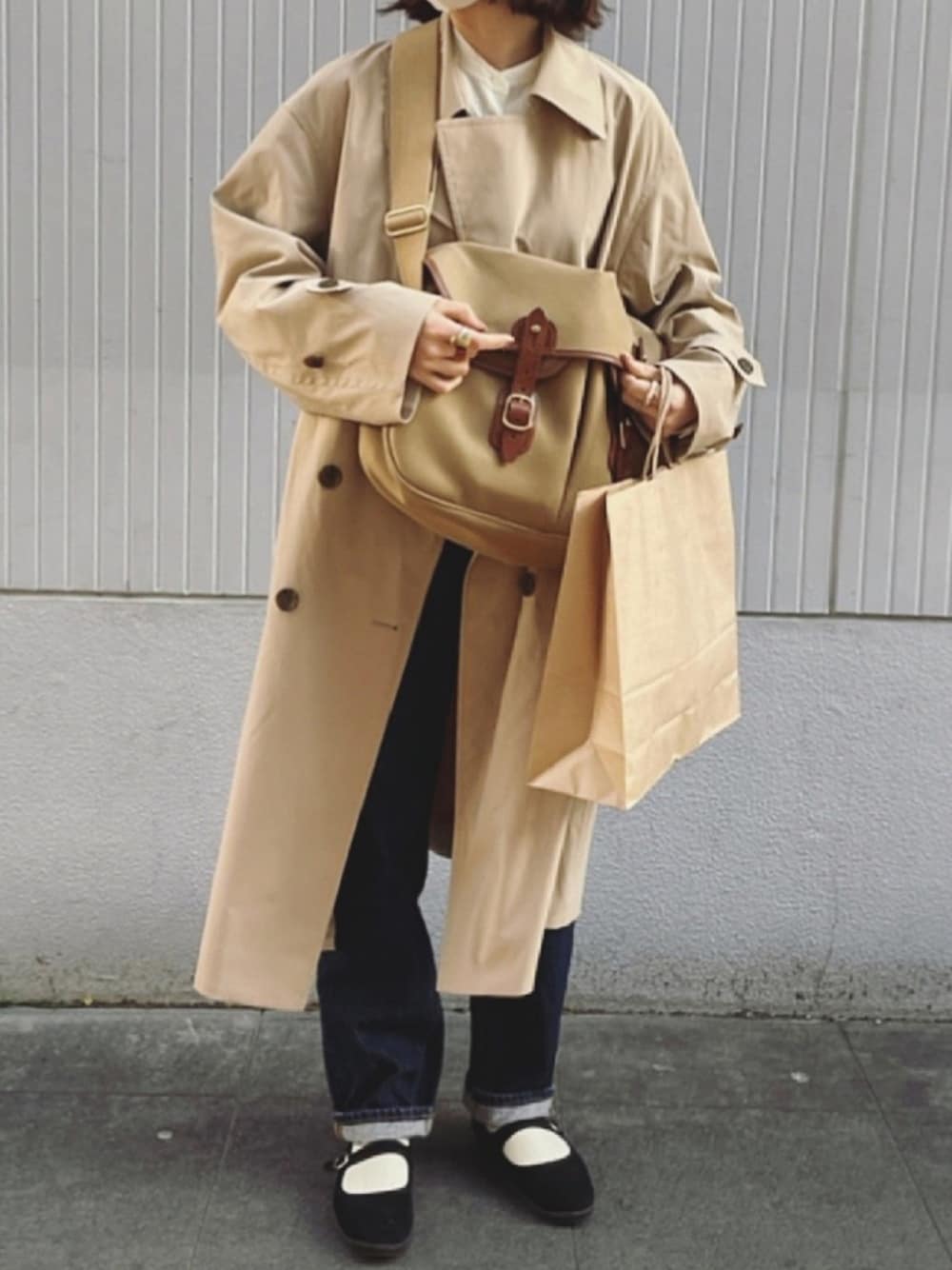 ベージュ系のトレンチコート、ベージュ系のショルダーバッグ、ブルー系のデニムパンツを着用したレディースの春コーディネートの1枚目の写真