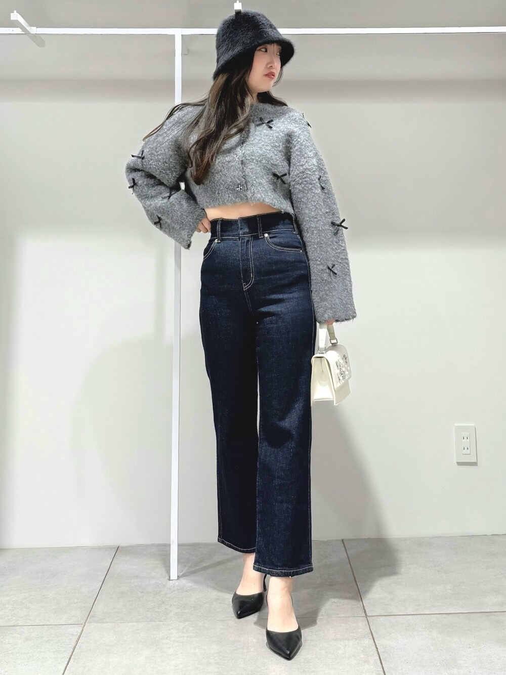 グレー系のカーディガン/ボレロ、ブルー系のデニムパンツ、ホワイト系のショルダーバッグを着用したレディースの冬コーディネートの1枚目の写真