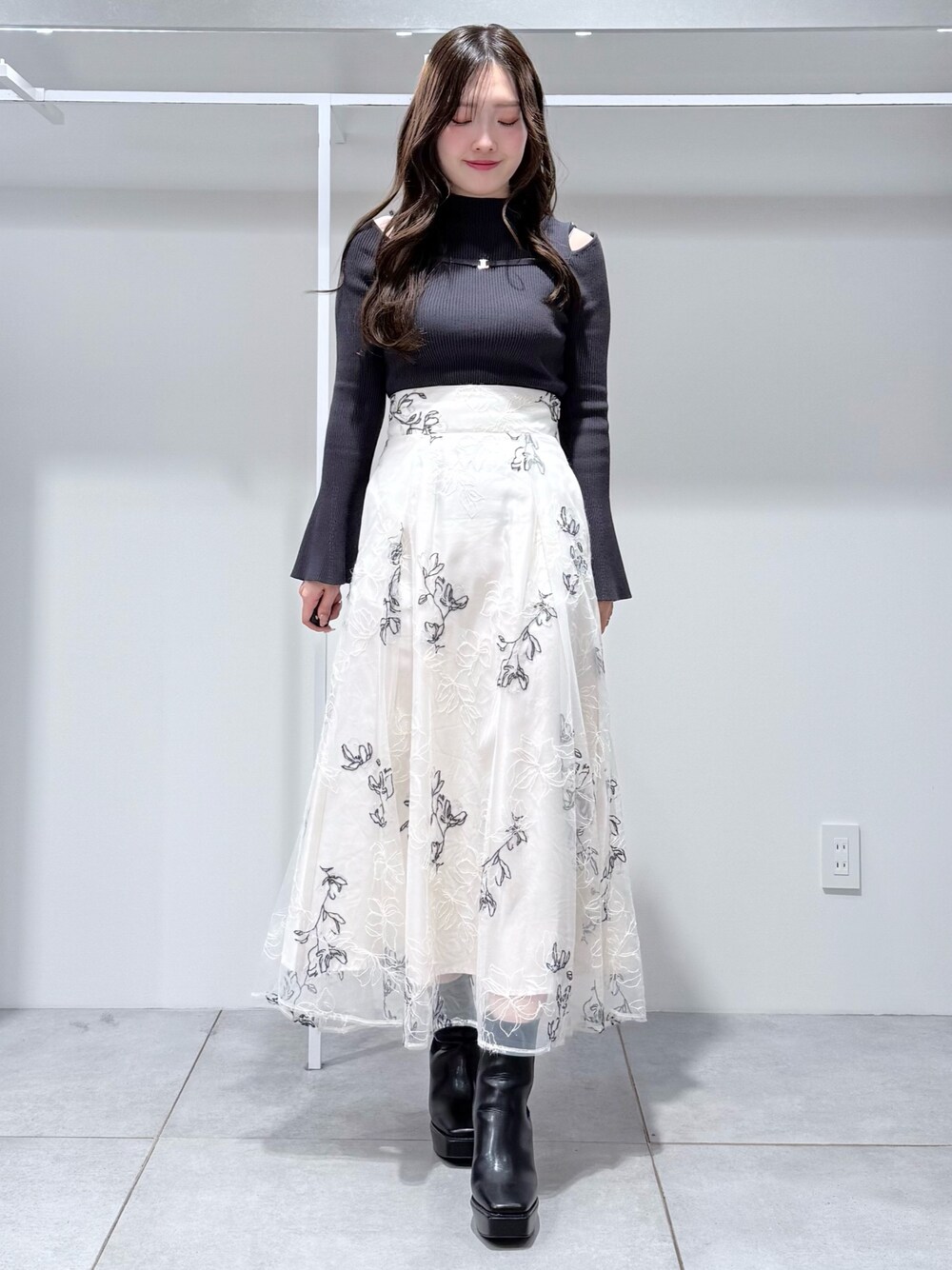 グレー系のニット/セーター、ブラック系のブーツ、ホワイト系のスカートを着用したレディースの冬コーディネートの1枚目の写真