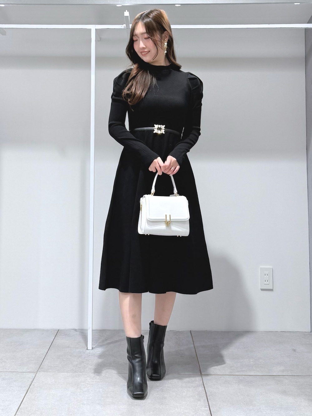 ホワイト系のハンドバッグ、ブラック系のブーツ、ブラック系のワンピースを着用したレディースの冬コーディネートの1枚目の写真