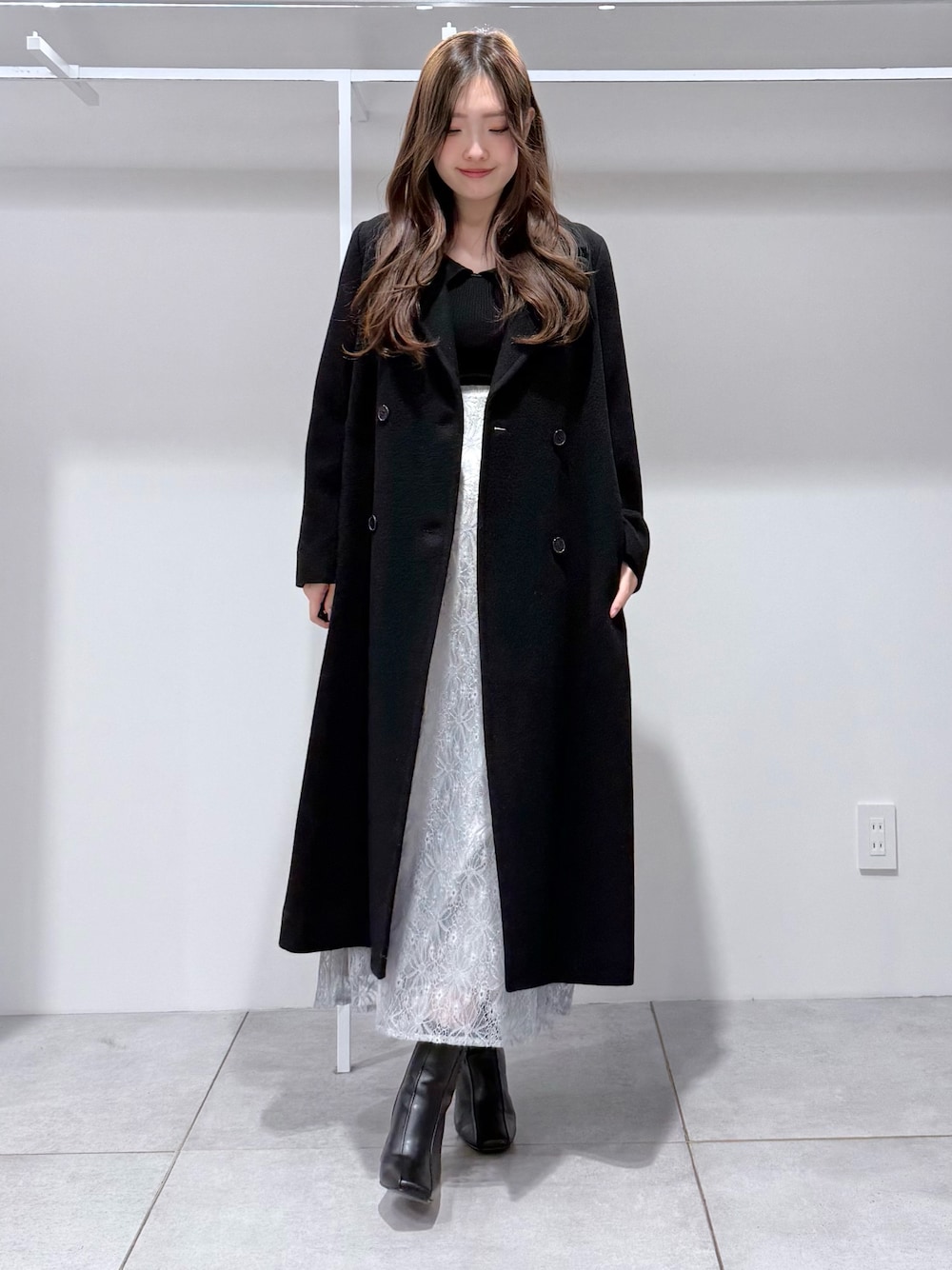 ブラック系のチェスターコート、ブラック系のニット/セーター、ブルー系のスカートを着用したレディースの冬コーディネートの1枚目の写真