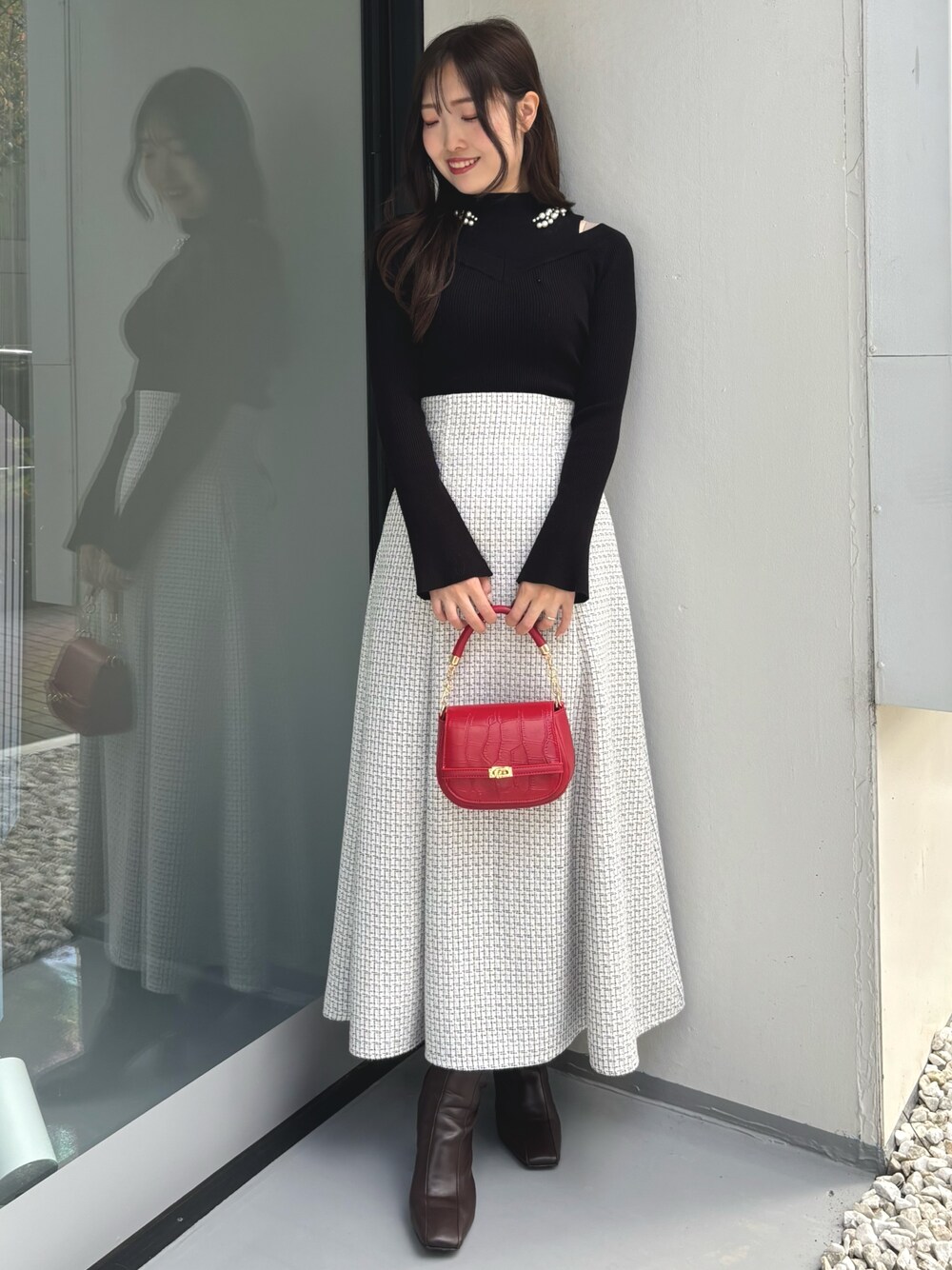 ブラック系のニット/セーター、レッド系のハンドバッグ、ホワイト系のスカートを着用したレディースの冬コーディネートの1枚目の写真