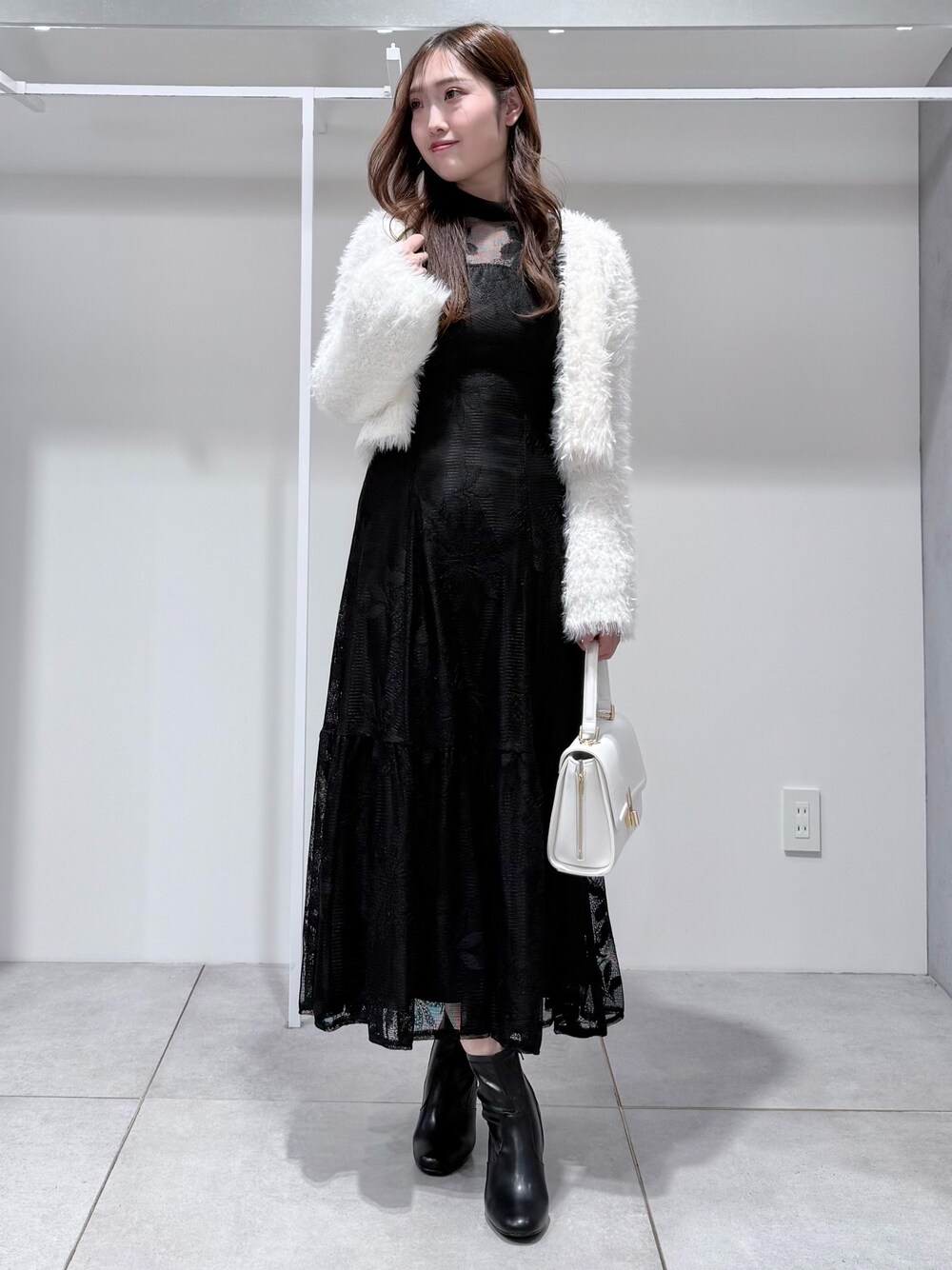 ブラック系のワンピース、ホワイト系のカーディガン/ボレロ、ホワイト系のハンドバッグを着用したレディースの冬コーディネートの1枚目の写真