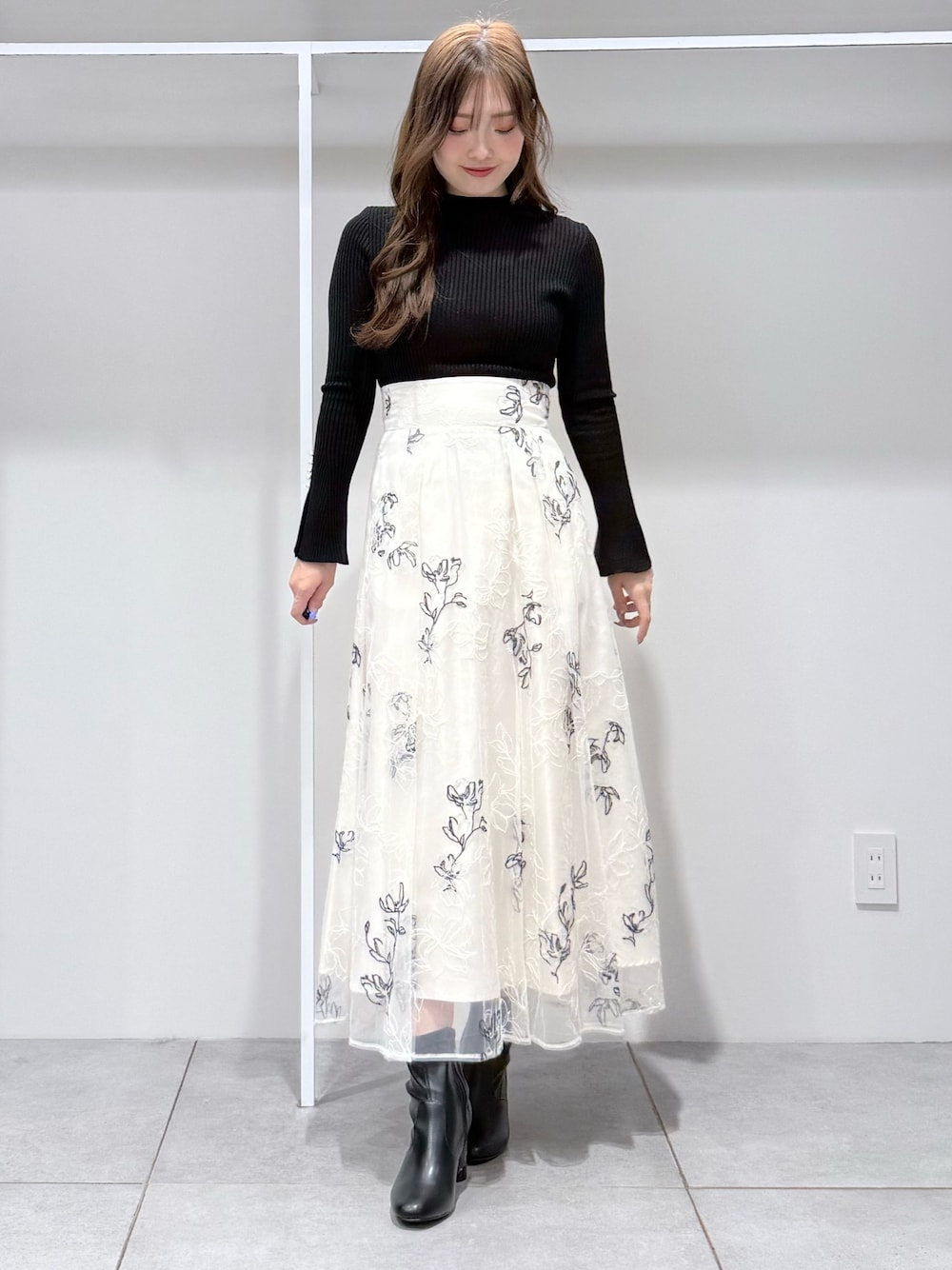 ブラック系のニット/セーター、ホワイト系のスカート、ブラック系のブーツを着用したレディースの冬コーディネートの1枚目の写真