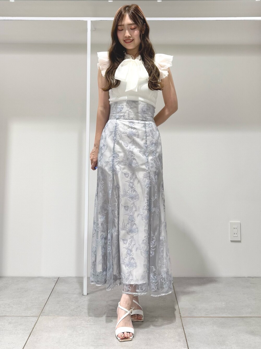 ホワイト系のニット/セーター、ブルー系のスカート、ホワイト系のサンダルを着用したレディースの春コーディネートの1枚目の写真