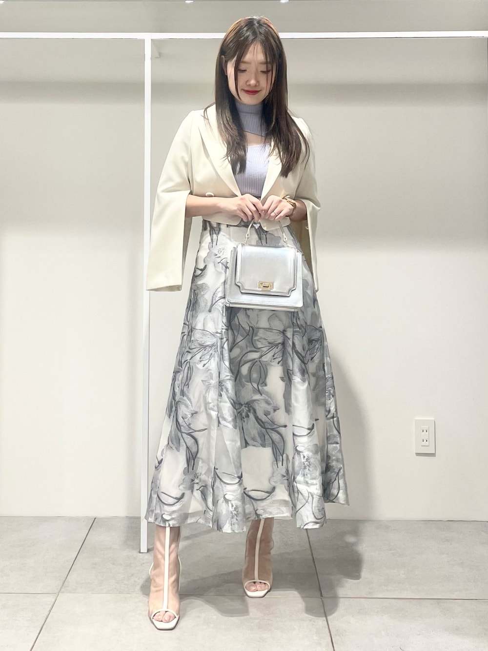 シルバー系のハンドバッグ、ホワイト系のテーラードジャケット、ブルー系のニット/セーターを着用したレディースの春コーディネートの1枚目の写真