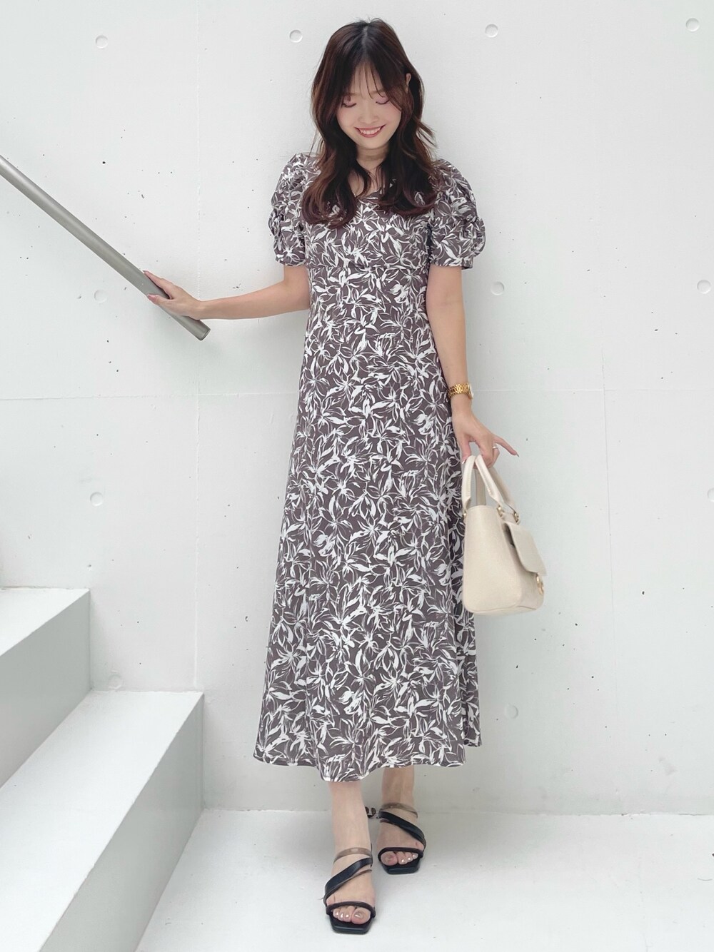 グレー系のワンピース、ブラック系のサンダル、ホワイト系のハンドバッグを着用したレディースの春コーディネートの1枚目の写真