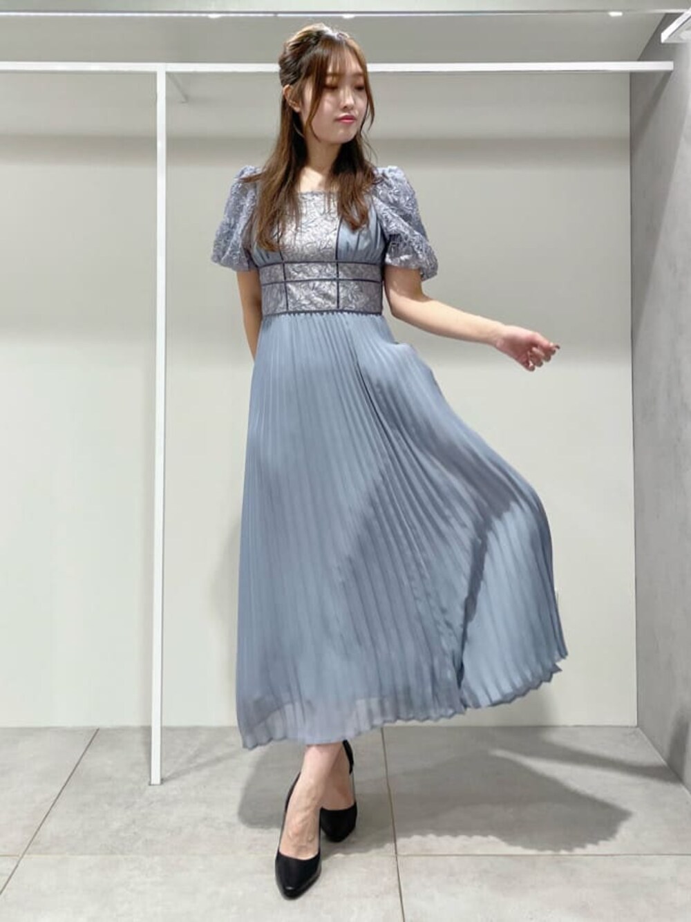 ブラック系のパンプス、ブルー系のワンピース、シルバー系のイヤリングを着用したレディースの秋コーディネートの1枚目の写真