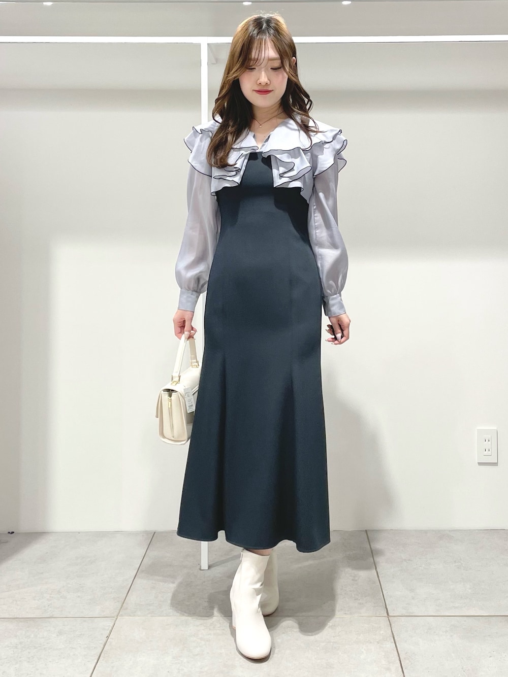 グレー系のワンピース、ホワイト系のブーツ、ホワイト系のハンドバッグを着用したレディースの冬コーディネートの1枚目の写真