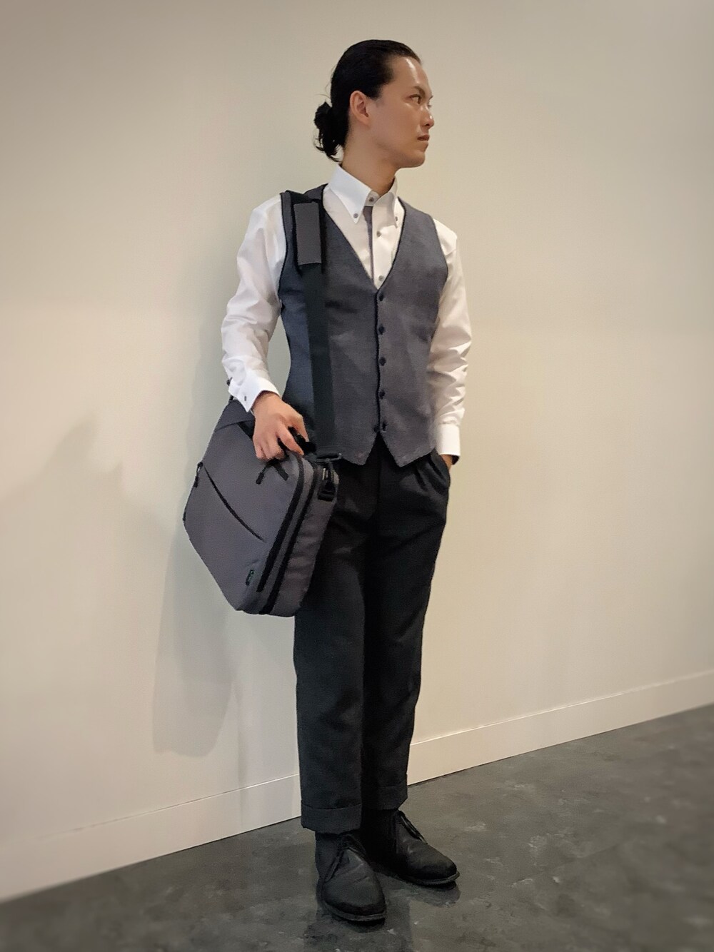 グレー系のベスト、ホワイト系のビジネスシャツ、グレー系のビジネスバッグを着用したメンズの秋コーディネートの1枚目の写真
