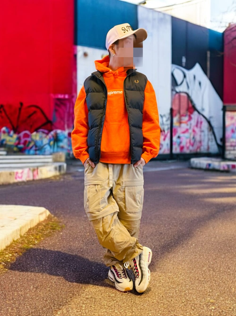 ブラック系のダウンベスト、オレンジ系のパーカー、ベージュ系のカーゴパンツを着用したメンズの秋コーディネートの1枚目の写真
