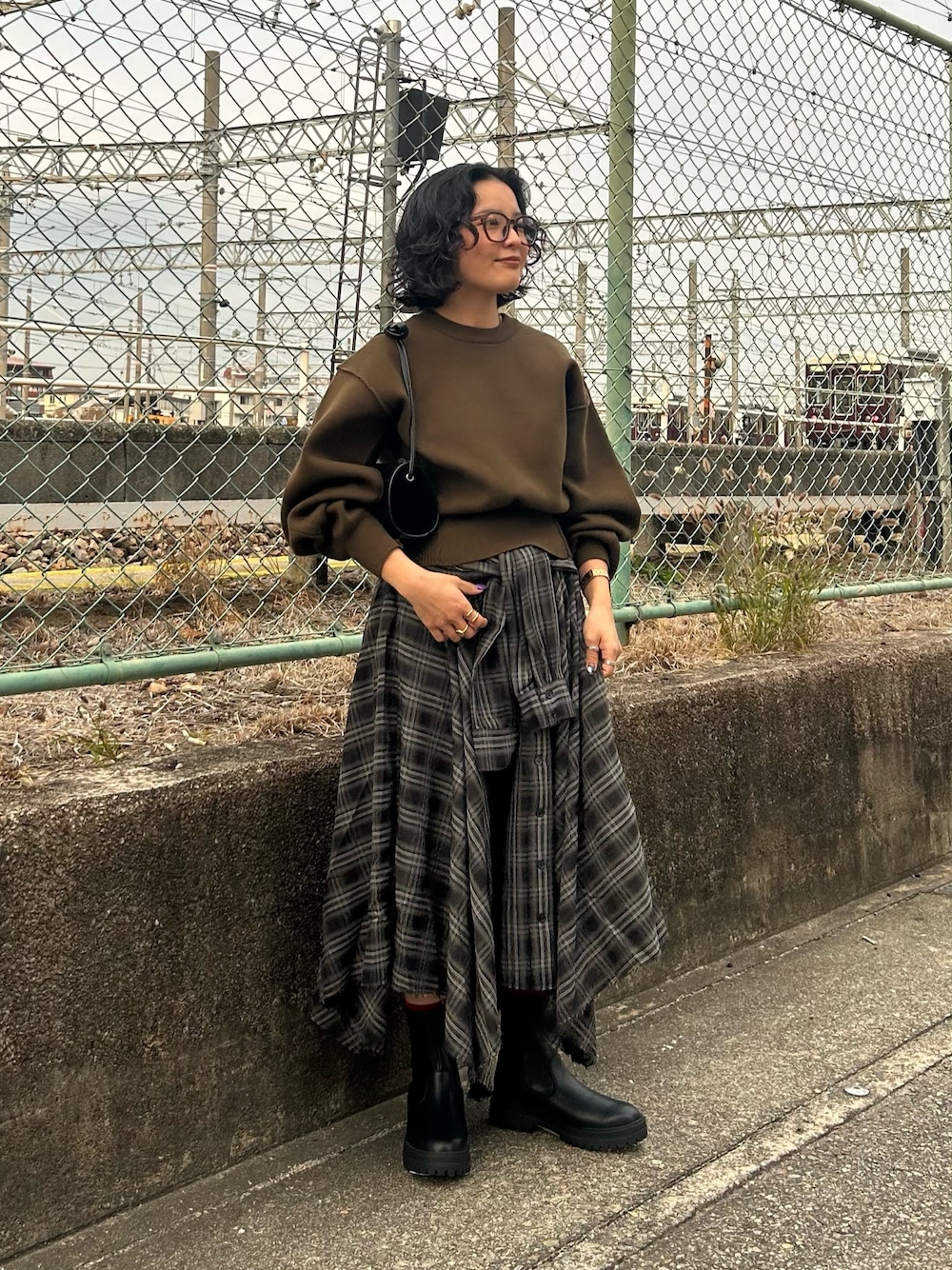 グリーン系のニット/セーター、ブラック系のスカート、ブラック系のブーツを着用したレディースの冬コーディネートの1枚目の写真