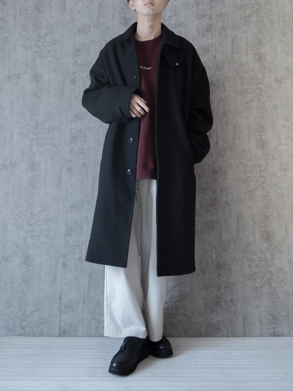 ブラック系のステンカラーコート、ホワイト系のスラックスを着用したメンズの冬コーディネートの1枚目の写真