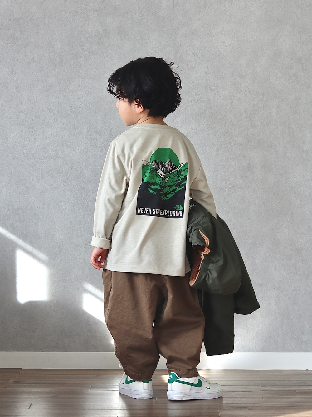 グリーン系のブルゾン、ベージュ系のTシャツ/カットソー、ブラウン系のチノパンツを着用したキッズの冬コーディネートの1枚目の写真