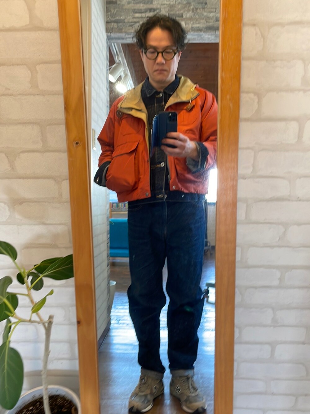 ブルー系のデニムジャケット、オレンジ系のマウンテンパーカー、ブルー系のデニムパンツを着用したメンズの春コーディネートの1枚目の写真