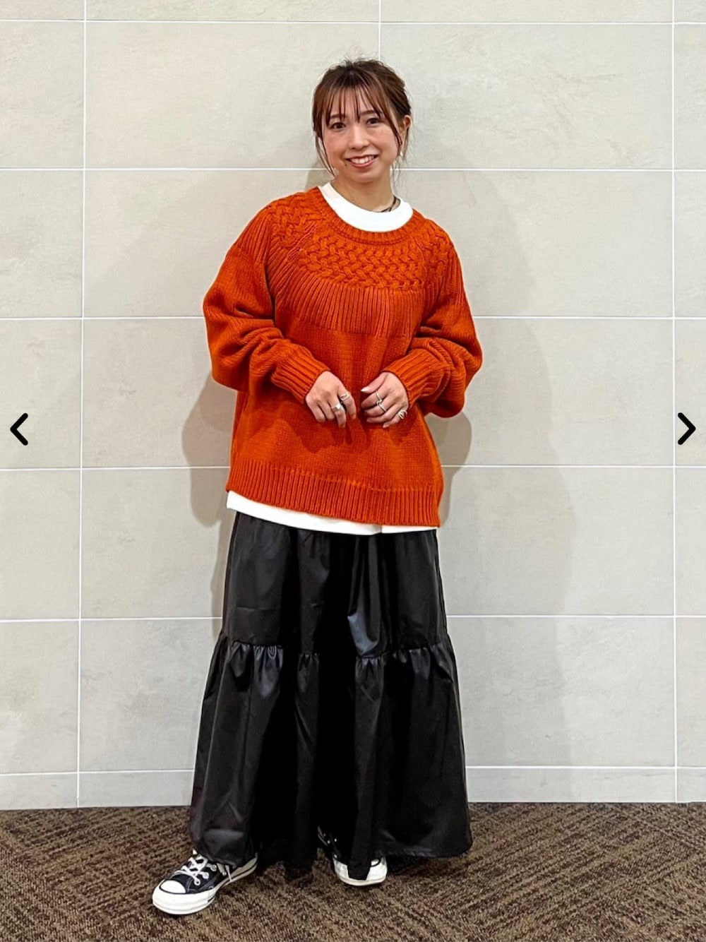 オレンジ系のニット/セーター、ブラック系のスカートを着用したレディースの秋コーディネートの1枚目の写真