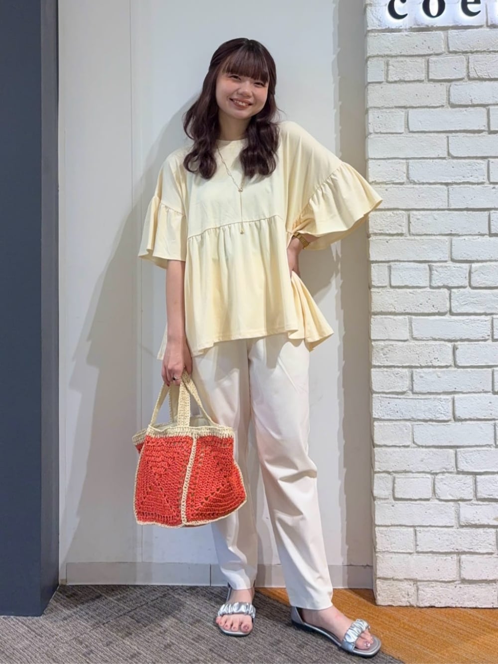 シルバー系のサンダル、オレンジ系のトートバッグ、ベージュ系のTシャツ/カットソーを着用したレディースの夏コーディネートの1枚目の写真