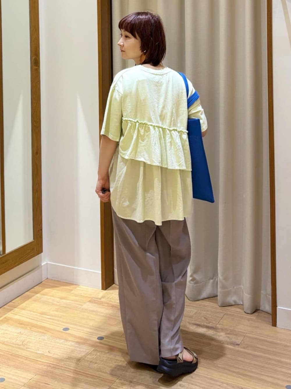 グレー系のスラックス、ベージュ系のサンダル、グリーン系のTシャツ/カットソーを着用したレディースの夏コーディネートの1枚目の写真