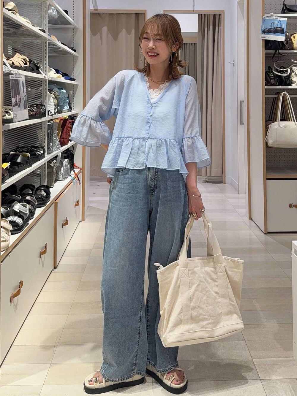 ホワイト系のトートバッグ、ブルー系のデニムパンツ、ホワイト系のサンダルを着用したレディースの春コーディネートの1枚目の写真