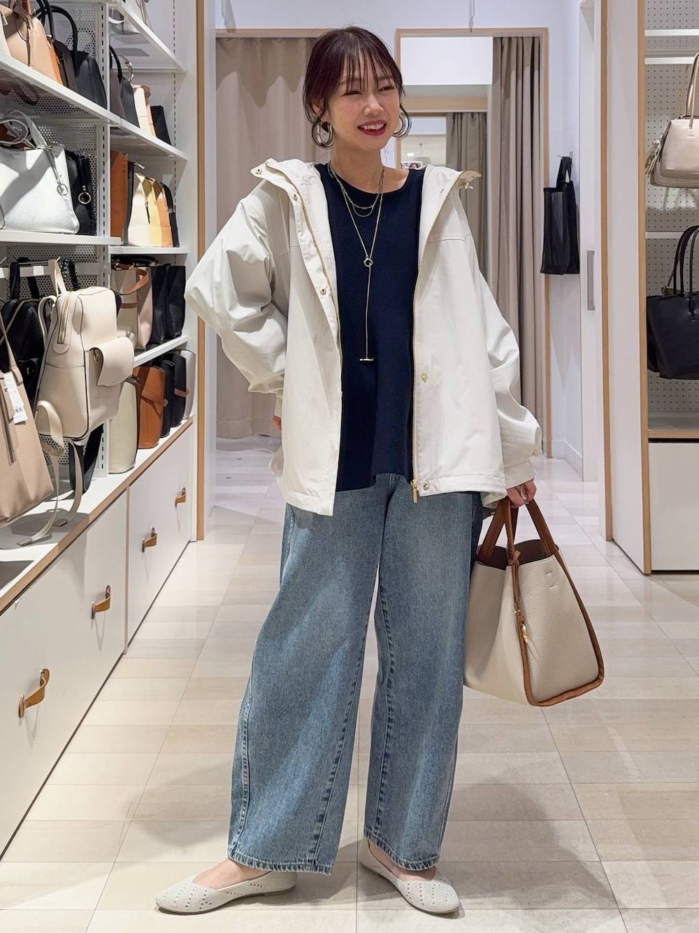 ベージュ系のトートバッグ、ベージュ系のマウンテンパーカー、ブルー系のデニムパンツを着用したレディースの春コーディネートの1枚目の写真