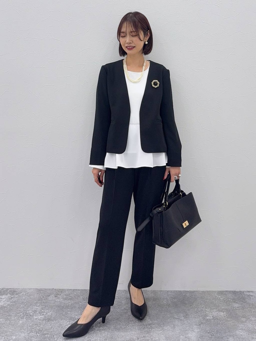 ブラック系のパンプス、ブラック系のセットアップ、その他のネックレスを着用したレディースの秋コーディネートの1枚目の写真