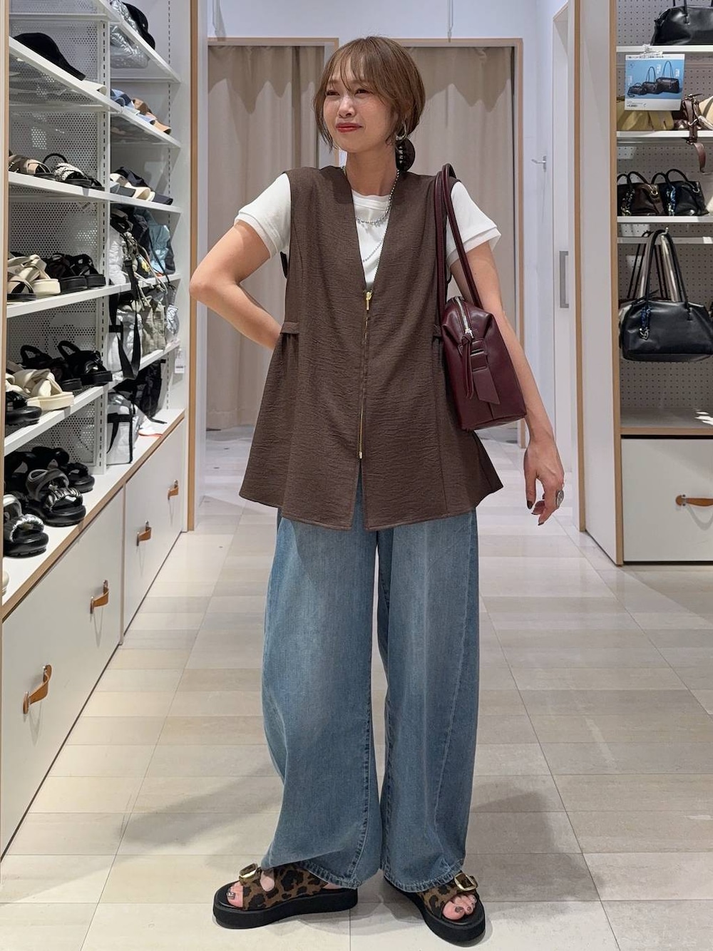 レッド系のボストンバッグ、ブルー系のデニムパンツ、ブラウン系のベストを着用したレディースの夏コーディネートの1枚目の写真