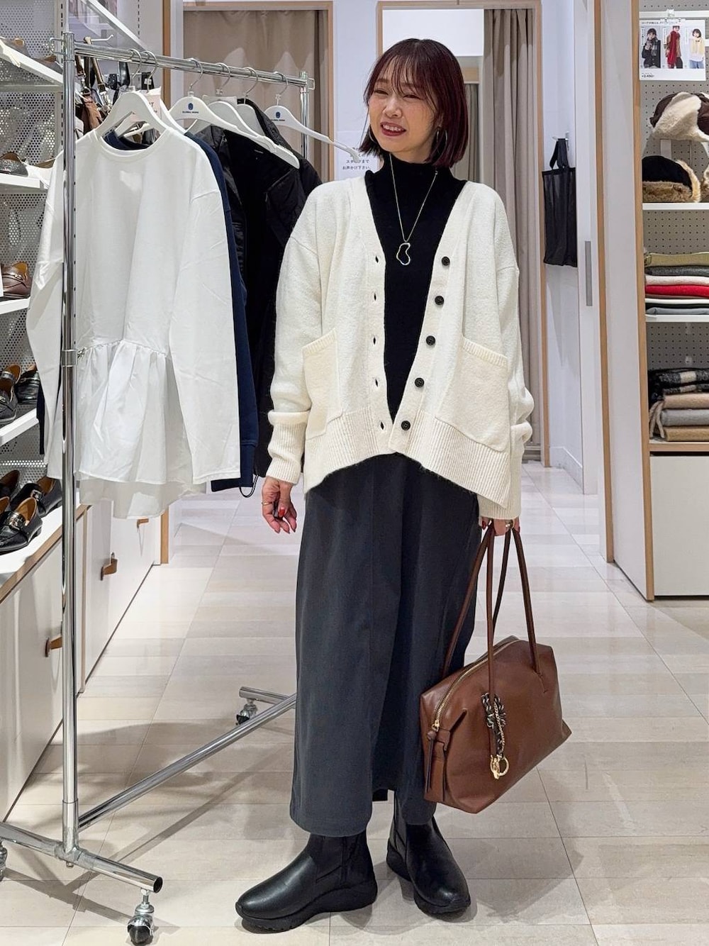 ブラウン系のボストンバッグ、ホワイト系のカーディガン/ボレロ、グレー系のスカートを着用したレディースの秋コーディネートの1枚目の写真