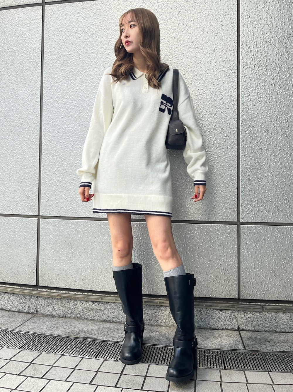 グレー系のハンドバッグ、ブラック系のブーツ、ホワイト系のニット/セーターを着用したレディースの冬コーディネートの1枚目の写真