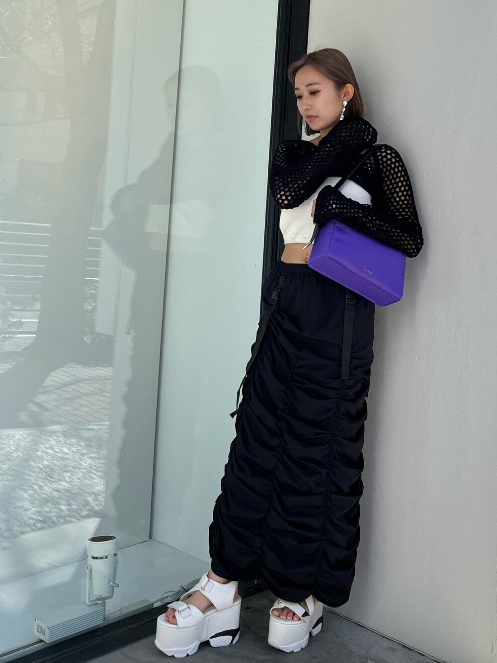 ブラック系のスカート、ブラック系のニット/セーター、パープル系のハンドバッグを着用したレディースの春コーディネートの1枚目の写真