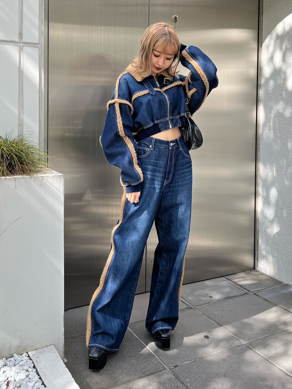 ブラック系のショルダーバッグ、ブラック系のブーツ、ブルー系のデニムパンツを着用したレディースの秋コーディネートの1枚目の写真