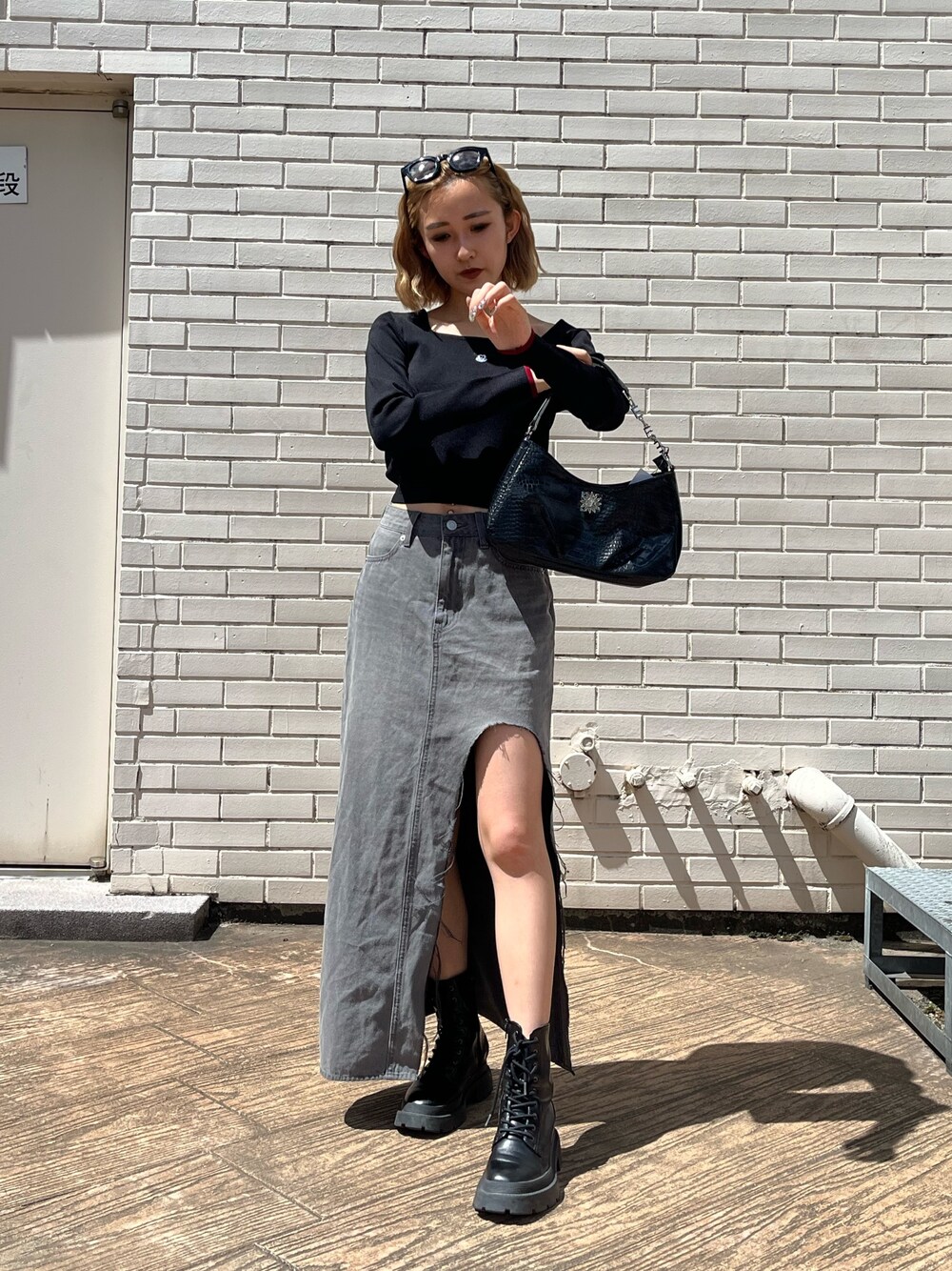 ブラック系のデニムスカート、ブラック系のブーツ、ブラック系のハンドバッグを着用したレディースの夏コーディネートの1枚目の写真