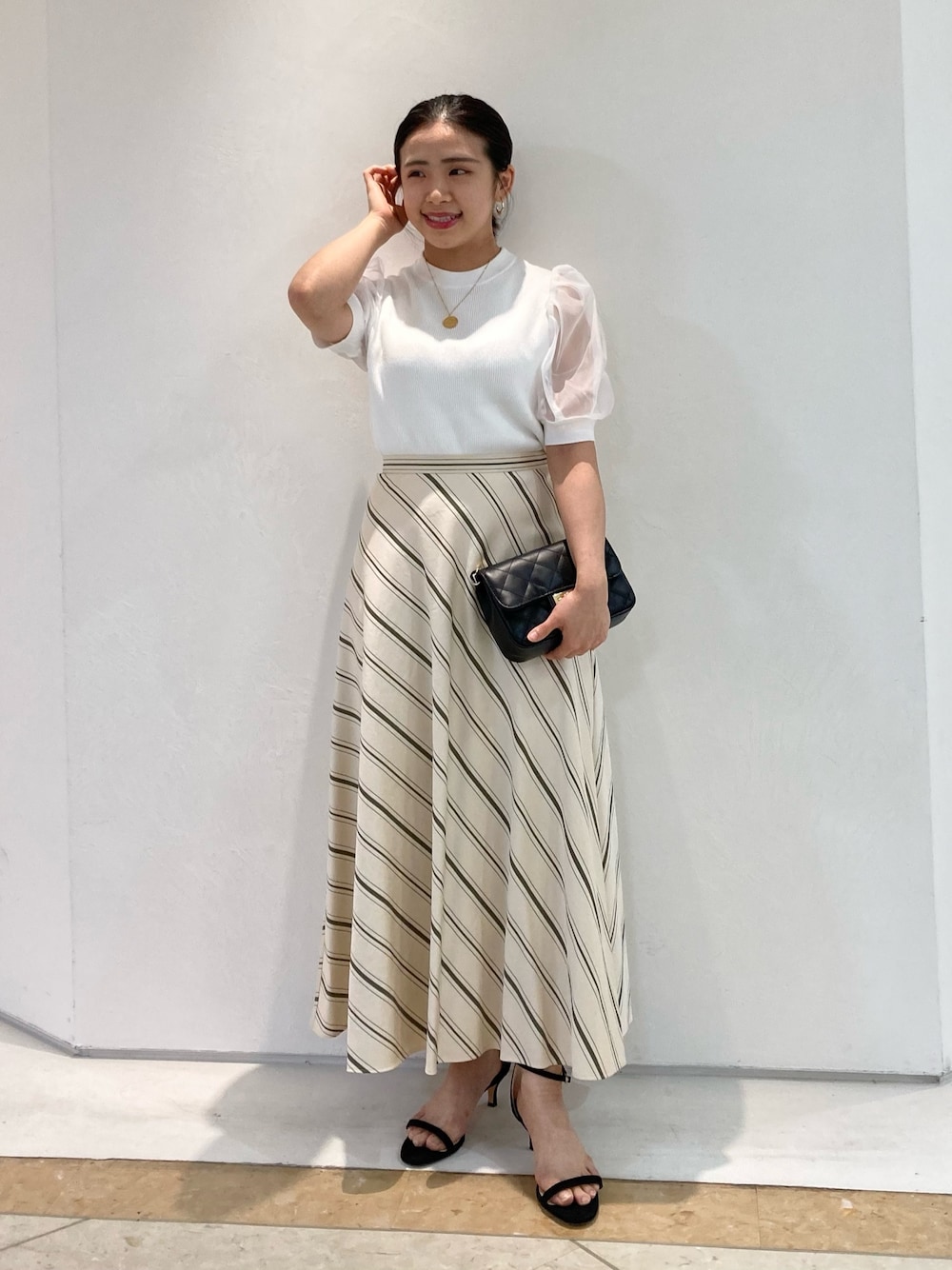 ブラック系のショルダーバッグ、ベージュ系のスカート、ブラック系のサンダルを着用したレディースの夏コーディネートの1枚目の写真