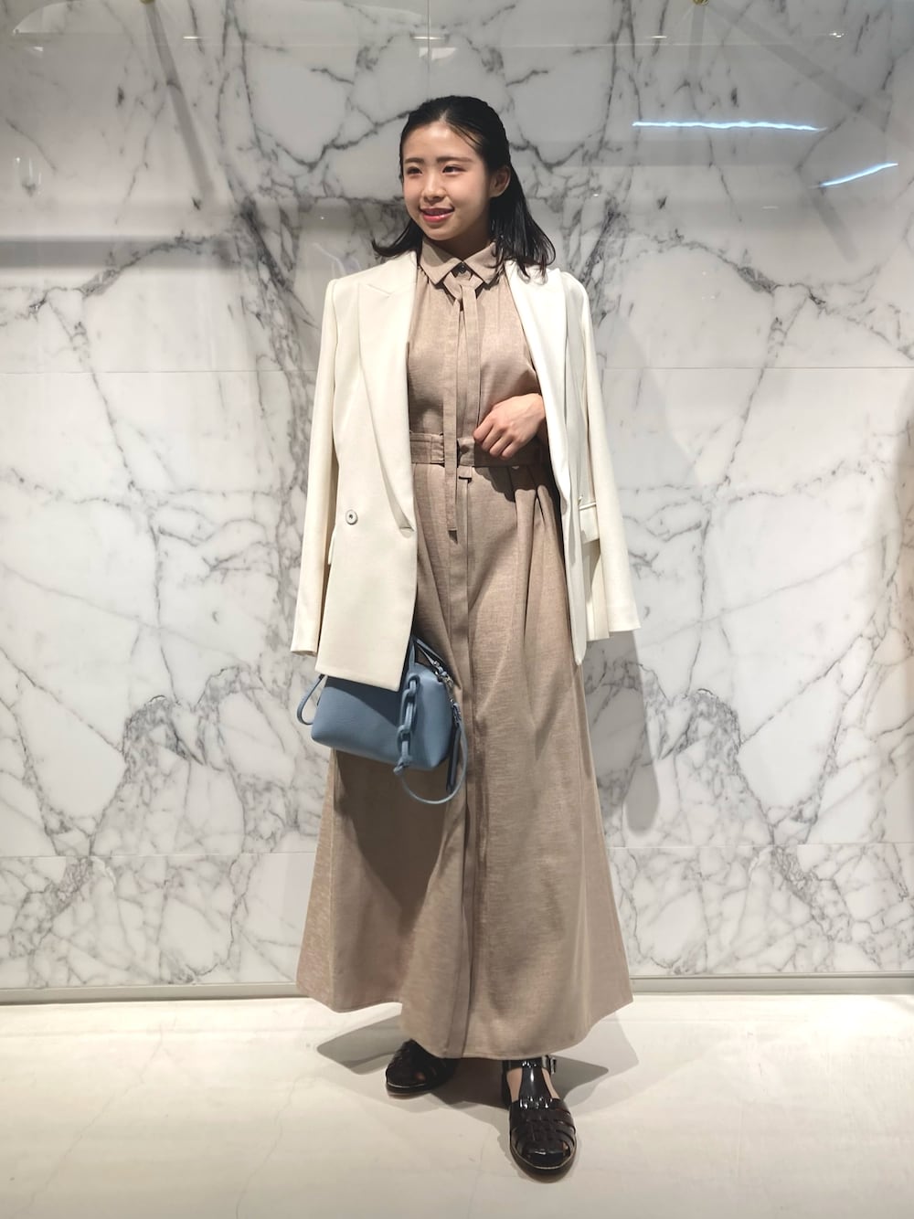 ベージュ系のシャツワンピース、ホワイト系のテーラードジャケット、ブルー系のショルダーバッグを着用したレディースの春コーディネートの1枚目の写真