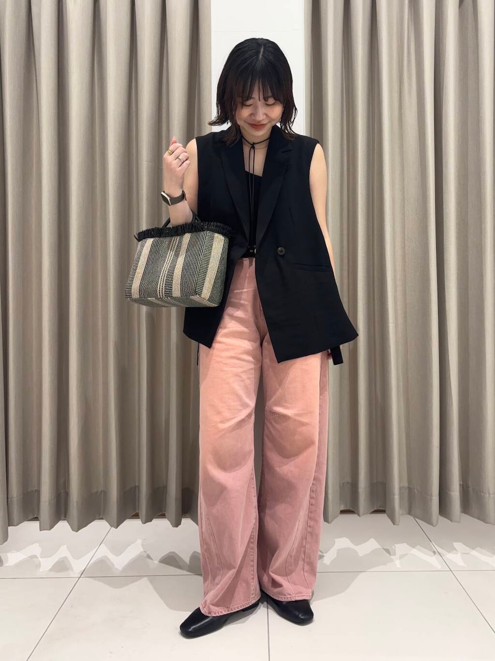 ピンク系のデニムパンツ、ブラック系のベスト、ブラック系のショルダーバッグを着用したレディースの春コーディネートの1枚目の写真