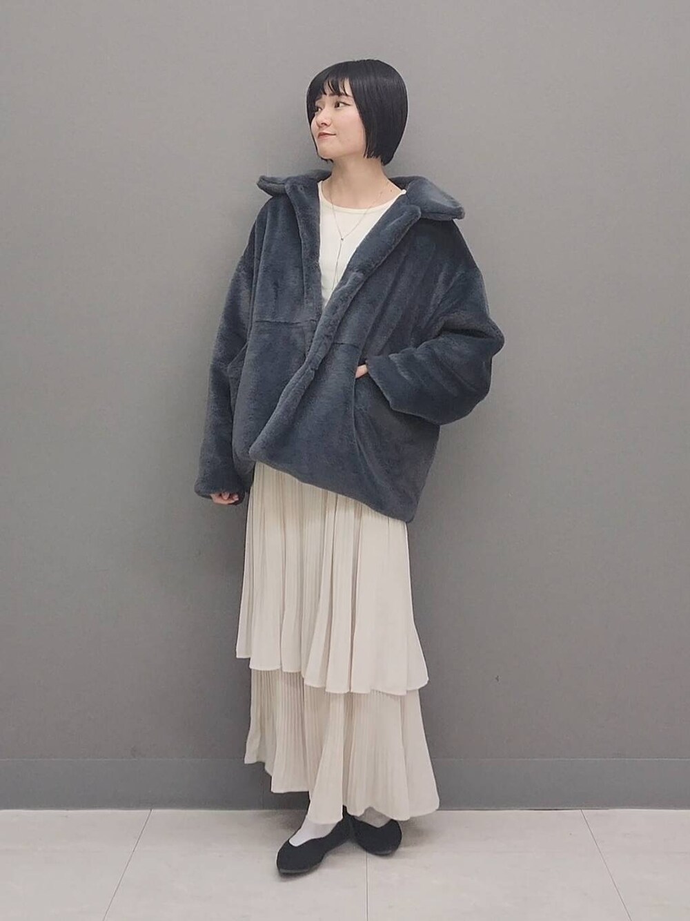 ベージュ系のスカート、グレー系のその他アウター、ホワイト系のニット/セーターを着用したレディースの冬コーディネートの1枚目の写真