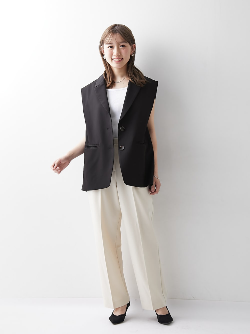 ホワイト系のスラックス、ブラック系のベスト、ホワイト系のキャミソールを着用したレディースの春コーディネートの1枚目の写真