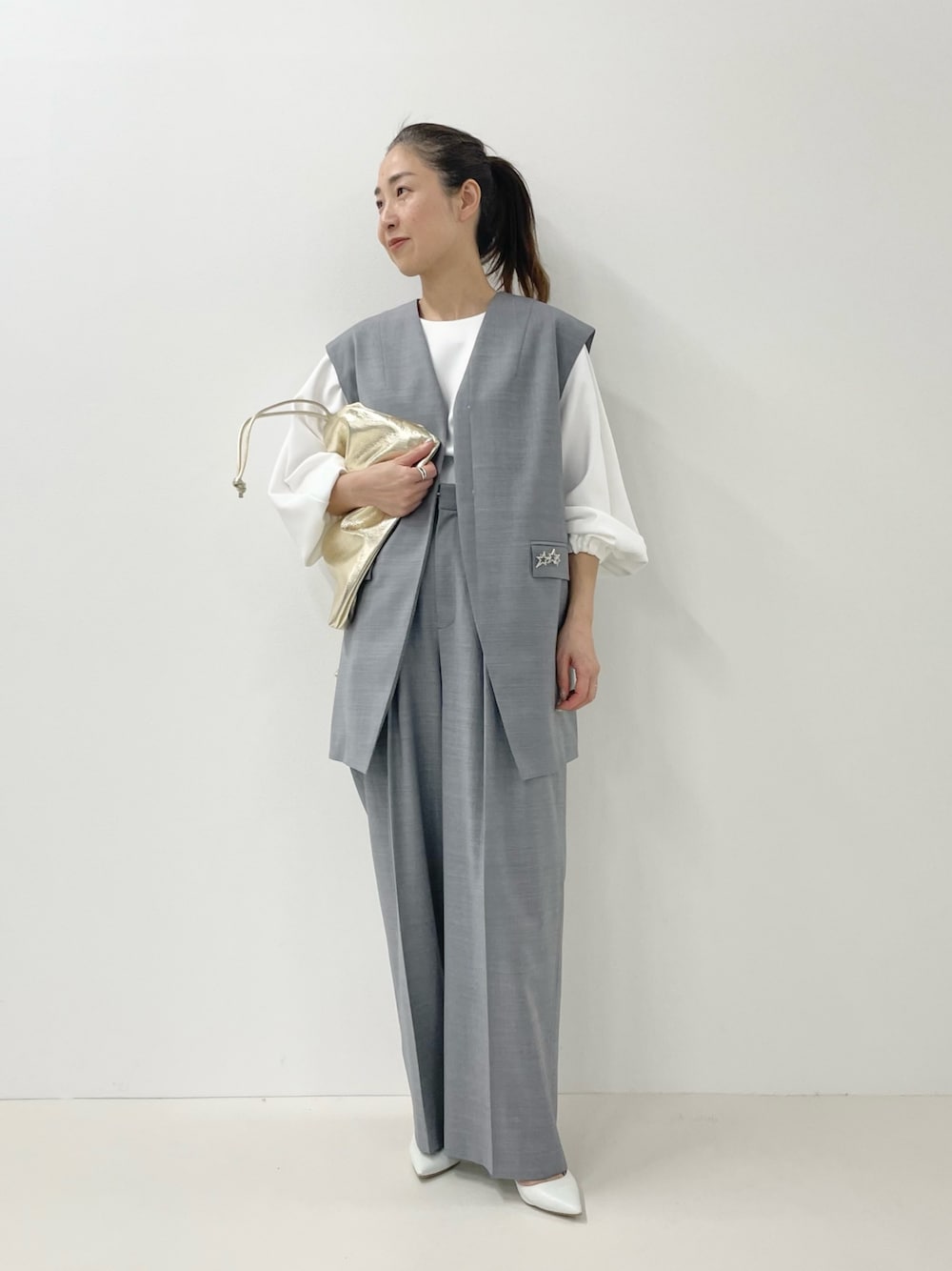 ゴールド系のショルダーバッグ、ホワイト系のTシャツ/カットソー、グレー系のベストを着用したレディースの冬コーディネートの1枚目の写真
