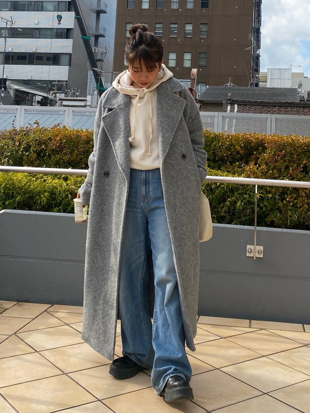 グレー系のチェスターコート、ホワイト系のパーカー、ブルー系のデニムパンツを着用したレディースの冬コーディネートの1枚目の写真