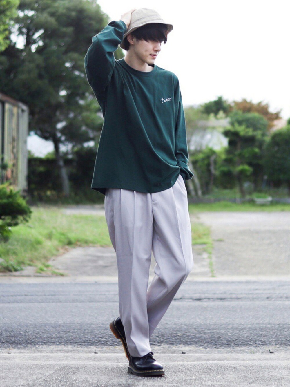 グリーン系のTシャツ/カットソー、ベージュ系のスラックス、ブラック系のブーツを着用したメンズの秋コーディネートの1枚目の写真