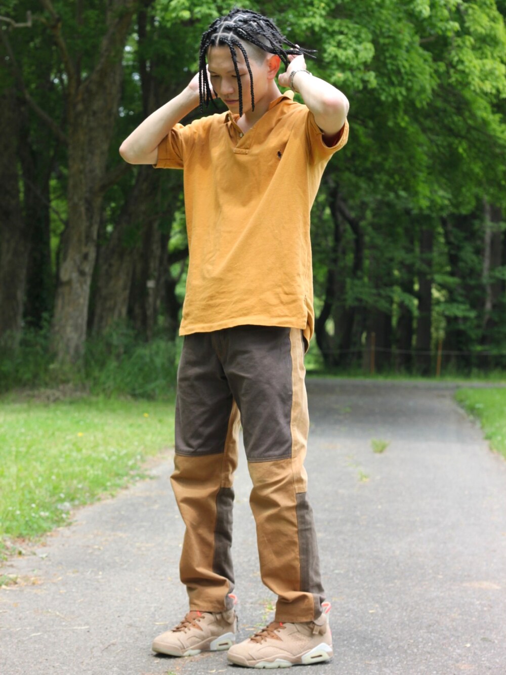 オレンジ系のポロシャツ、ブラウン系のデニムパンツ、ベージュ系のスニーカーを着用したメンズの春コーディネートの1枚目の写真